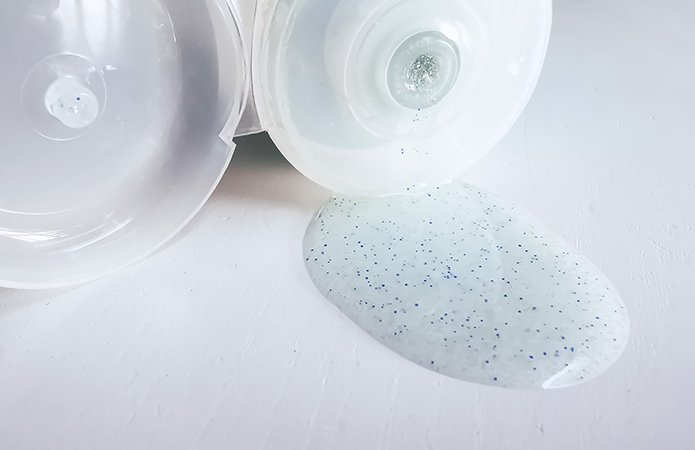 Gel cosmetico con microgranuli blu fuoriuscito da un flacone aperto su superficie bianca, simbolo dell'articolo del blog cosmetic and medical device di Lifeanalytics sulle Microplastiche nei cosmetici: normativa, analisi e impatti ambientali
