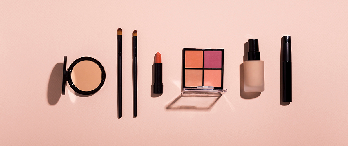 Set di cosmetici su sfondo rosa: cipria compatta, pennelli, rossetto, palette di ombretti, fondotinta e mascara disposti in ordine, simbolo dell'articolo del blog cosmetic and medical device di Lifeanalytics sulle Microplastiche nei cosmetici: normativa, analisi e impatti ambientali