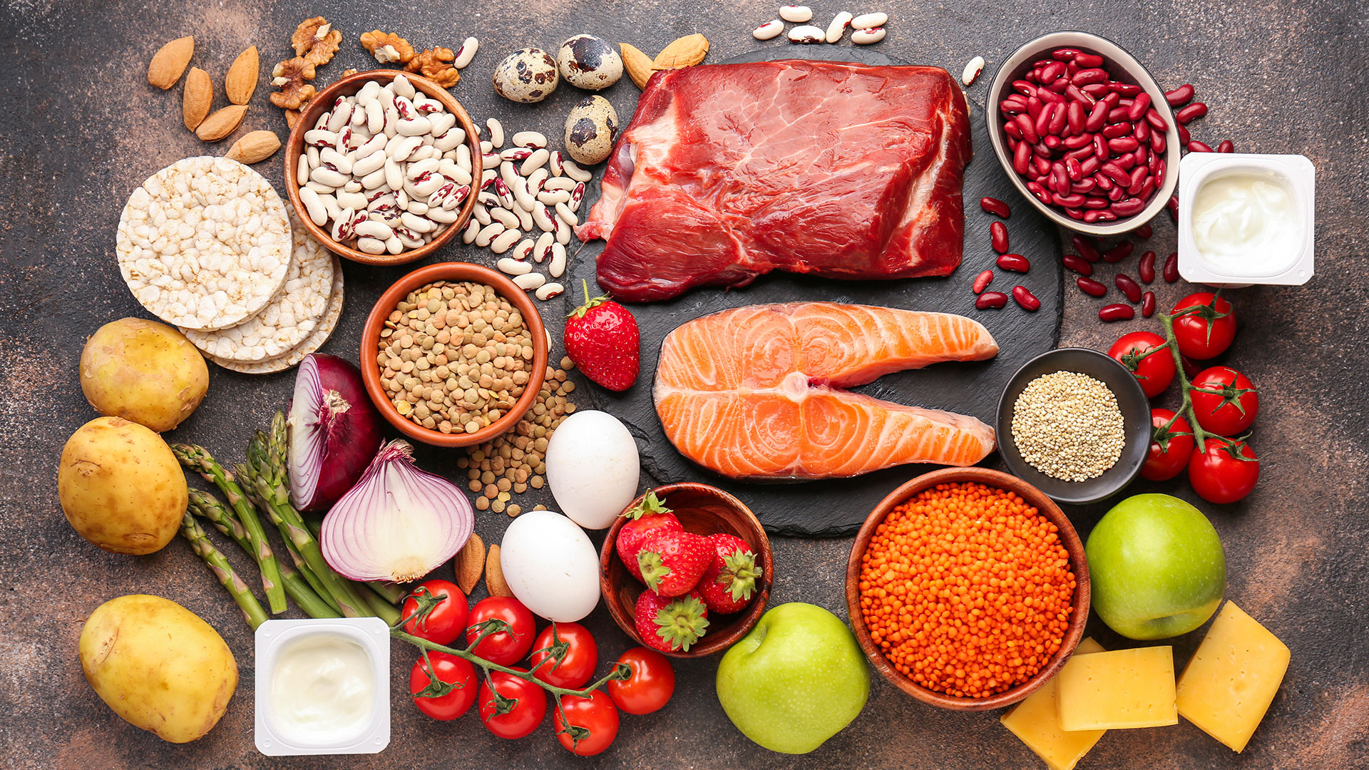 Alimenti vari su fondo scuro, tra cui carne, pesce, legumi, frutta, verdura, latticini e cereali, simbolo del servizio Alimenti Dietetici, Plant-Based e Vegan Food