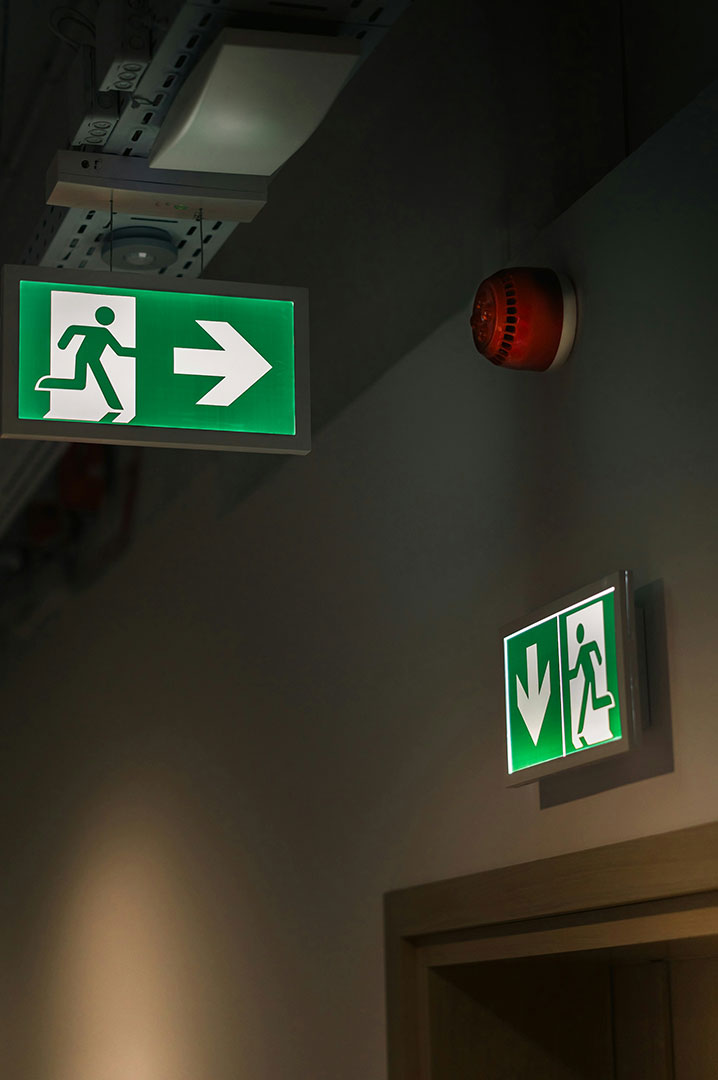 Segnaletica di emergenza illuminata con indicazioni di uscita e direzione di evacuazione in un ambiente interno.