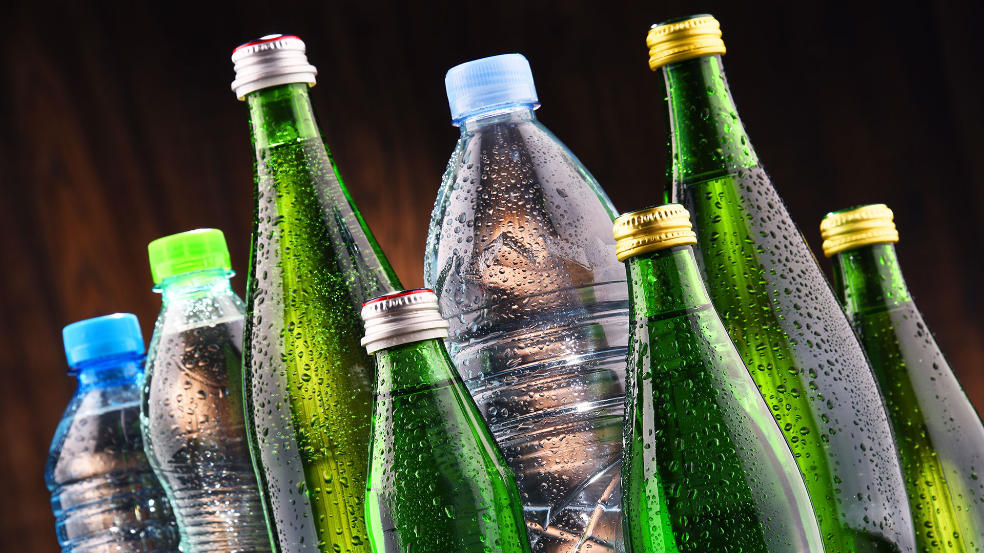 Bottiglie di acqua in plastica e vetro con gocce di condensa su sfondo scuro