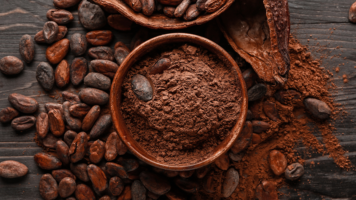 Ciotola di legno piena di cacao in polvere circondata da fave di cacao e bucce su fondo di legno scuro, simbolo del servizio Caffè, olio, uova, cacao e grassi alimentari della business unit food di Lifeanalytics