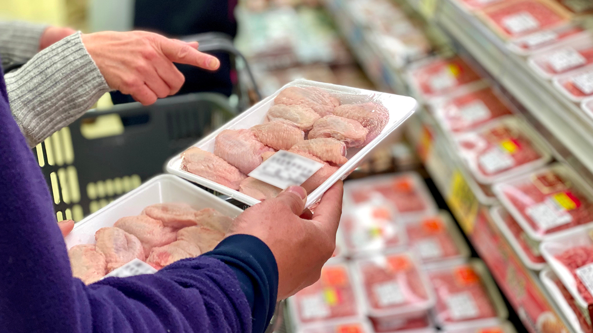 Persone che osservano confezioni di carne cruda in vaschetta al supermercato, davanti a un banco frigo, simbolo del servizio carne e derivati della business unit food di Lifeanalytics