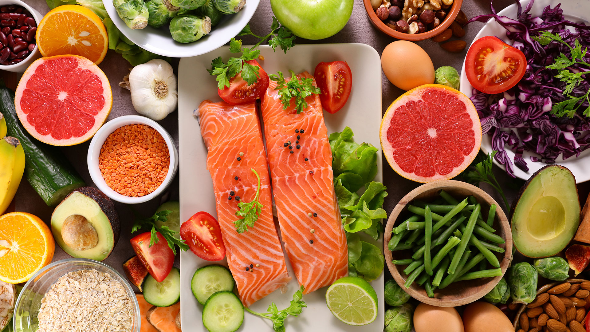 Immagine di una vista dall’alto di filetti di salmone circondati da frutta, verdura, legumi, uova e cereali, rappresentazione di alimentazione sana ed equilibrata, simbolo di qualità e sicurezza alimentare, simbolo del corso dedicato alle certificazioni Kosher e Halal