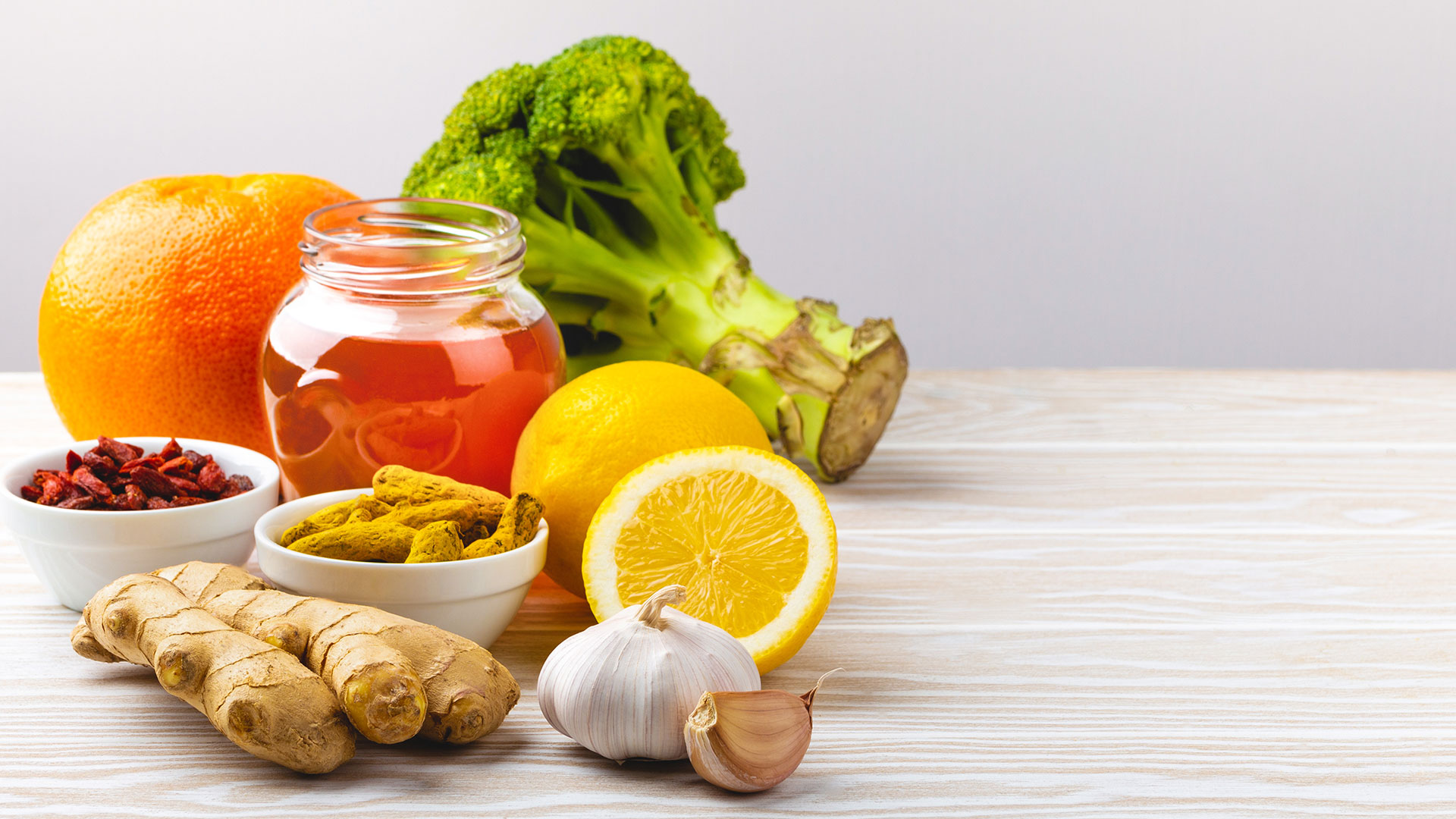 Immagine di alimenti naturali su piano da lavoro in legno: miele in barattolo, arancia, limone, broccoli, aglio, zenzero, bacche di goji e spezie, simbolo del corso dedicato alla Food fraud & food defence