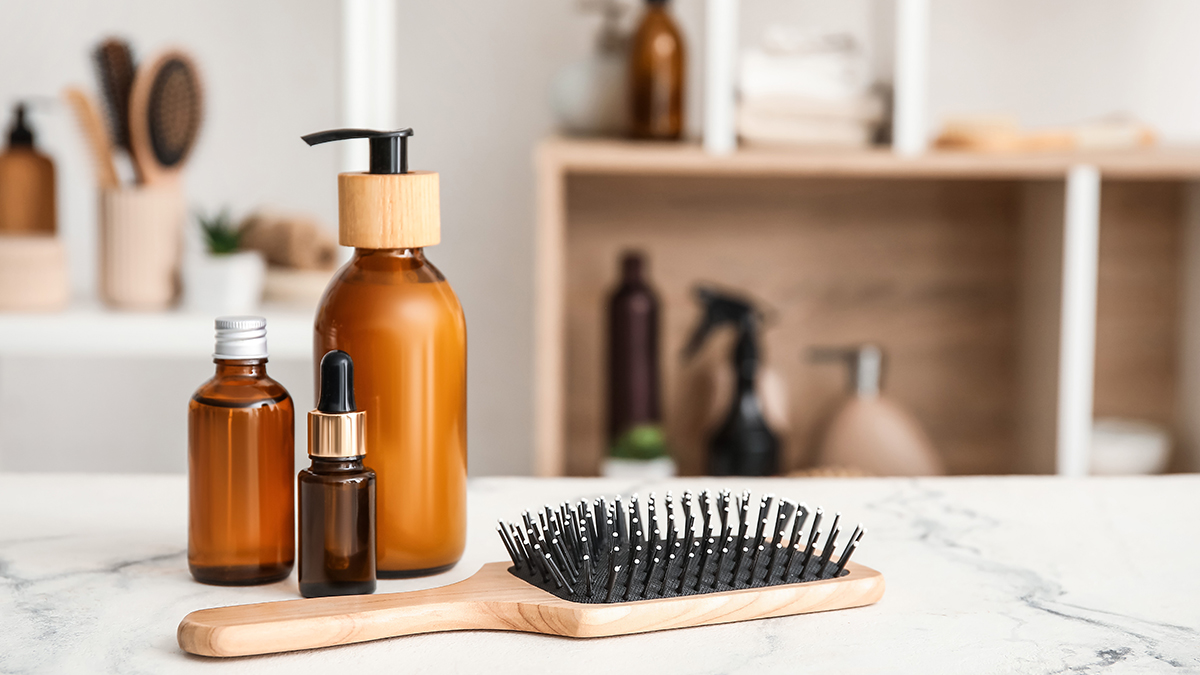 Haircare product set with amber bottles and a wooden brush on a marble surface in a minimalist bathroom setting, representing the Haircare service of the cosmetic and medical device business unit of Lifeanalytics.