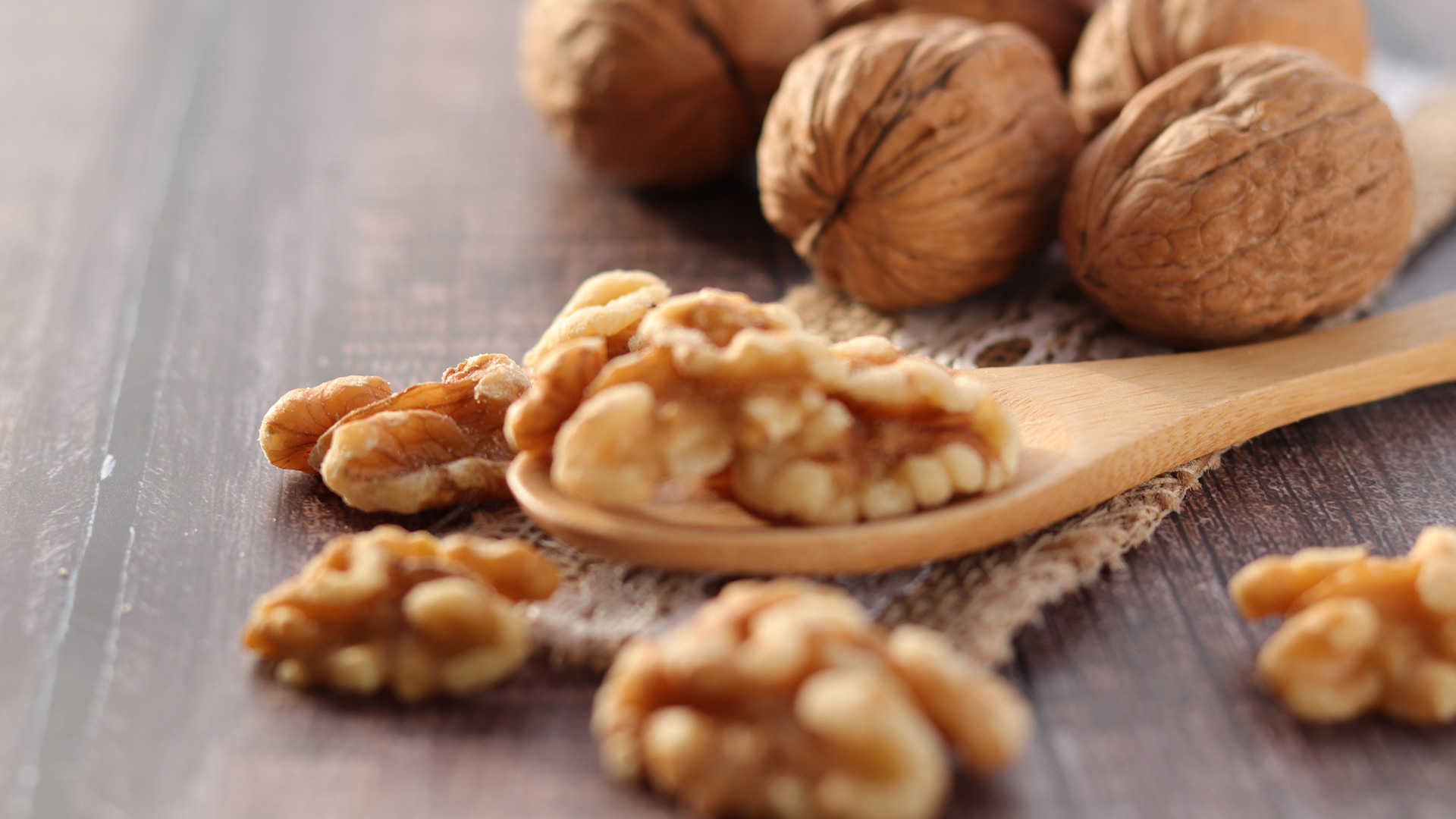 Walnut kernels on a wooden spoon with whole walnuts in the background, symbolizing Lifeanalytics' dried fruit and tree nuts service