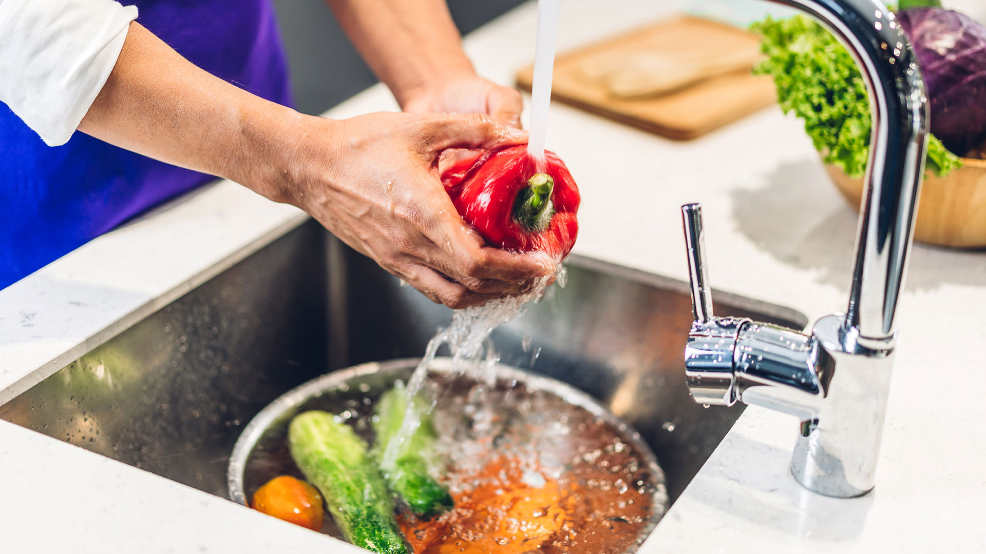 Immagine di una persona che lava peperoni e verdure sotto acqua corrente nel lavello della cucina, pratica di igiene alimentare e sicurezza alimentare, simbolo del corso dedicato all'igiene degli alimenti e la loro contaminazione