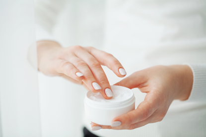 Mani femminili che prelevano crema da un barattolo bianco, concetto di skincare e cura della pelle