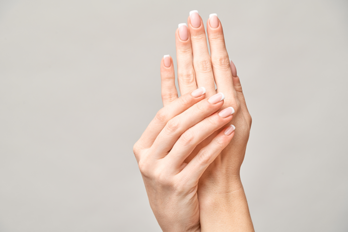 Mani femminili curate con manicure francese su sfondo neutro, in una posa elegante e delicata, simbolo dell'articolo del blog sul futuro degli smalti per le unghie dopo l’addio agli ingredienti proibiti TPO e DMTA