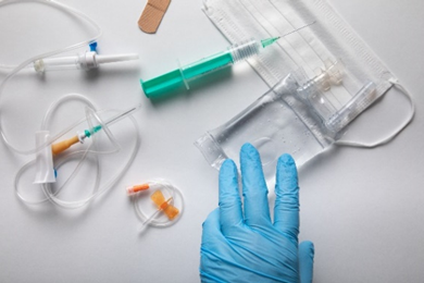 Immagine di un bancone con sopra dispositivi medici come mascherina, cerotto, fialette, aghi, siringhe e una mano con un guanto azzurro, simbolo dell’articolo dedicato alla Nuova ISO 10993-1, valutazione biologica dei dispositivi medici della business unit cosmetic & medical device di Lifeanalytics