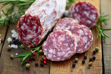 Salame nostrano disposto sopra un tavolo di legno con alcune fette tagliate, rosmarino e grano di pepe, simbolo di allerta per la presenza di Lysteria monocytogenes