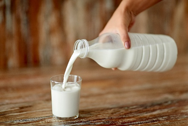 Immagine di una mano femminile intenta a versare latte fresco in un bicchiere da una bottiglia di plastica su un tavolo rustico in legno, simbolo dell'articolo del blog della business unit Food di Lifeanalytics dedicato alla listeria nei formaggi e delle recenti allerte che stanno aumentando l'attenzione sulla sicurezza alimentare