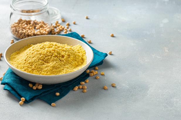 Piatto bianco in ceramica posizionato sopra un tavolo con tovagliolo blu, contenente farina di ceci e ceci secchi a fianco, ingrediente naturale per ricette salutari e alimentazione vegetariana, immagine simbolo del prodotto richiamato per presenza di Clorpirifos, un insetticida rigorosamente vietato nell’Unione Europea