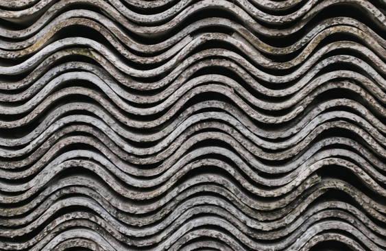 Lastre ondulate in cemento-amianto accatastate, potenziale fonte di esposizione alle fibre di amianto, immagine simbolica dell’articolo dedicato alle nuove regole del D.Lgs. 213/2025 per la gestione del rischio amianto e la prevenzione dell'esposizione nei luoghi di lavoro della business unit EHS