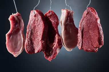 Immagine di una serie di tagli di carne bovina cruda sospesi tramite ganci da macelleria, illuminati su sfondo nero con effetto professionale, simbolo dell'articolo del blog della business unit Food di Lifeanalytics dedicato ai nitriti e nitrati, I nitriti, composti chimici derivati dall'acido nitroso e identificati negli alimenti principalmente come additivi E249 (nitrito di potassio) ed E250 (nitrito di sodio)