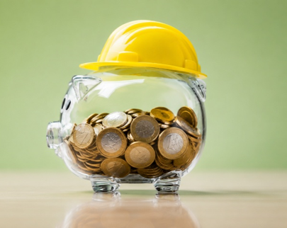 Salvadanaio in vetro pieno di monete con casco di sicurezza giallo, simbolo dell'articolo della business unit EHS dedicato al Conto Formazione, ai Fondi Interprofessionali e al finanziamento della formazione aziendale in materia di salute e sicurezza