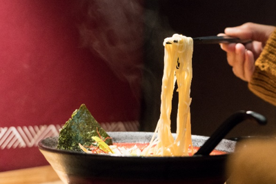 Immagine di una ciotola di ramen istantaneo caldo con noodles sollevati con le bacchette, simbolo di richiamo per produzione in uno stabilimento non autorizzato