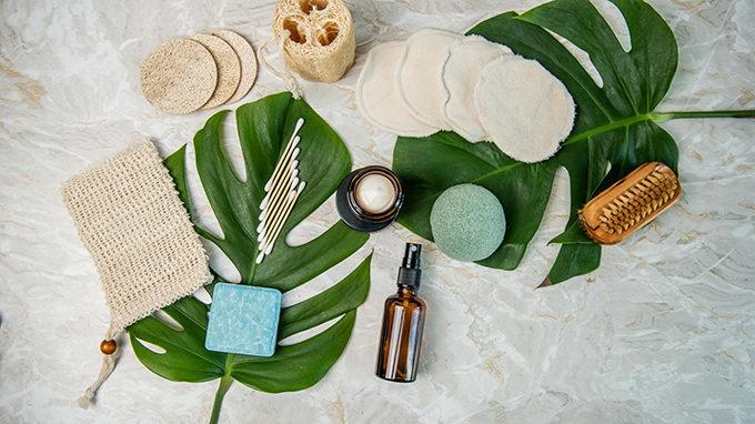 Prodotti cosmetici sostenibili e accessori riutilizzabili disposti su foglie di monstera, con imballaggi ecologici e materiali naturali, simbolo dell'articolo del blog cosmetic and medical device di Lifeanalytics sulla Sostenibilità: il rischio microbiologico nella cosmesi green