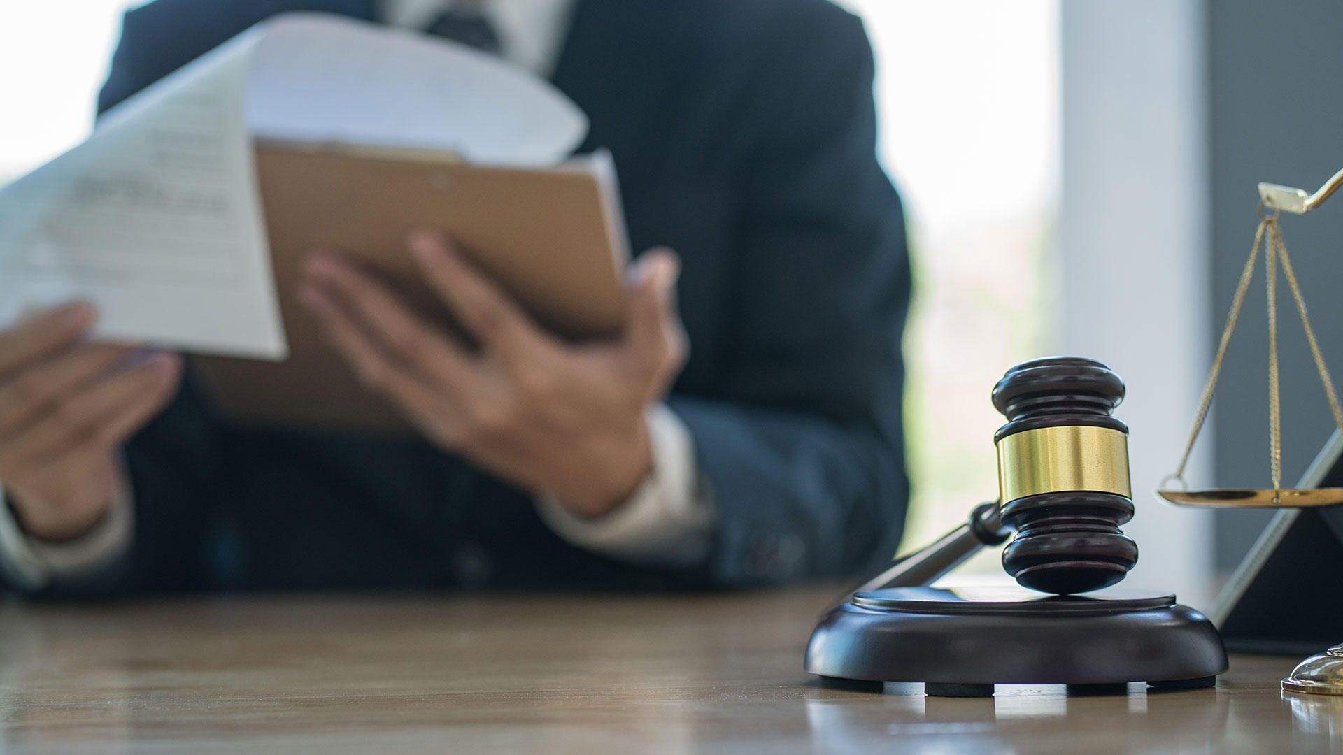 Immagine di una scrivania con oggetti legati alla legge come mantelletto, bilancia e plichi, simbolo del servizio dedicato all'implementazione sistemi normativa cogente 