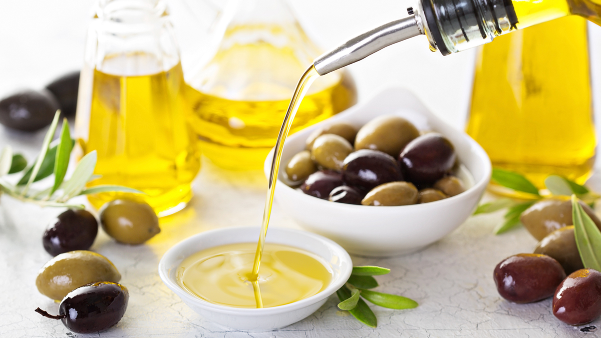 Olio d'oliva versato in una ciotolina bianca, circondato da olive verdi e nere, bottiglie di olio e rami di ulivo, simbolo del servizio Caffè, olio, uova, cacao e grassi alimentari della business unit food di Lifeanalytics