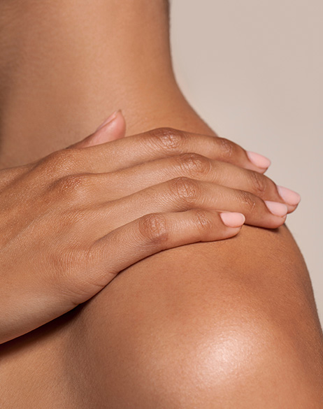 primo piano di una mano appoggiata sulla spalla nuda di una persona, con pelle liscia e curata su sfondo neutro, simbolo della prevenzione dell’invecchiamento della pelle