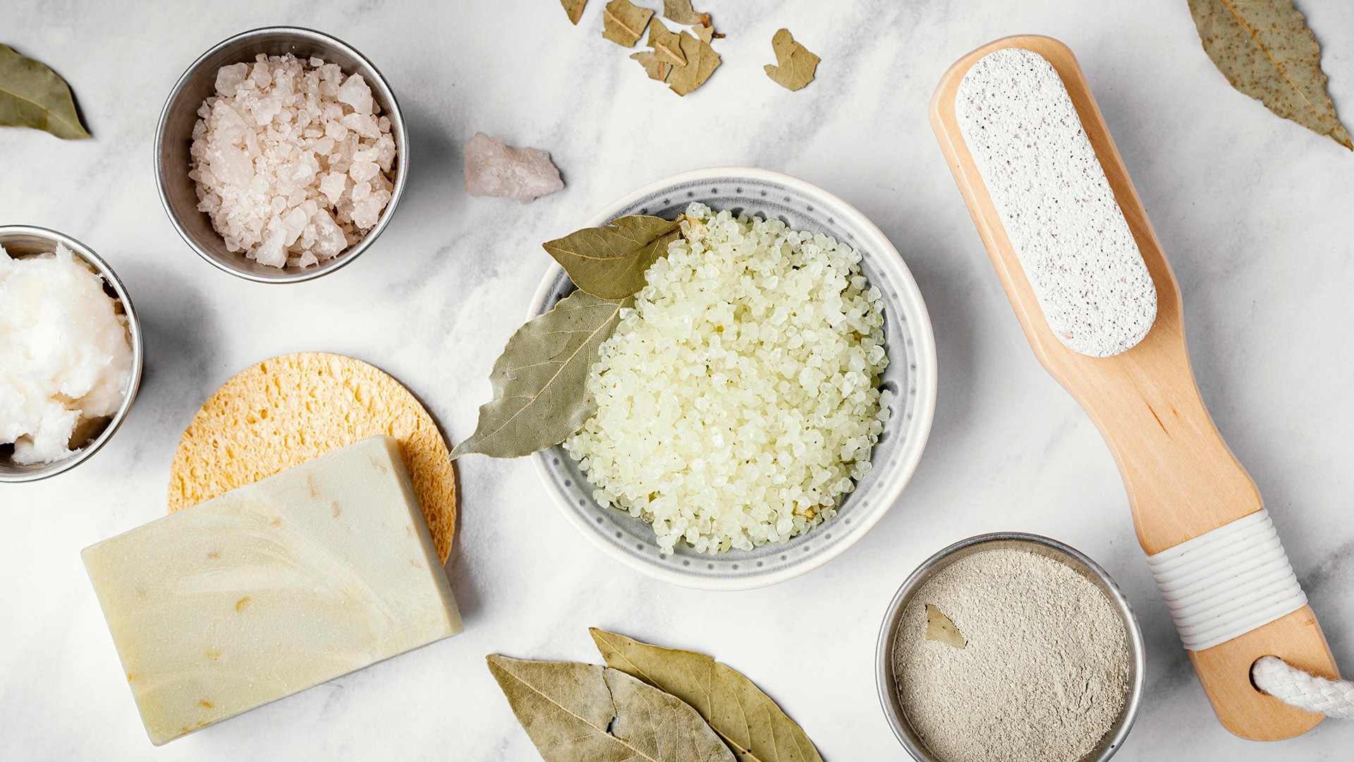 Ingredienti naturali e prodotti skincare su fondo di marmo: sali, sapone, foglie di alloro, pietra pomice, e argilla per scrub e trattamenti di bellezza, simbolo del servizio Raw material della business unit cosmetic and medical device di Lifeanalytics