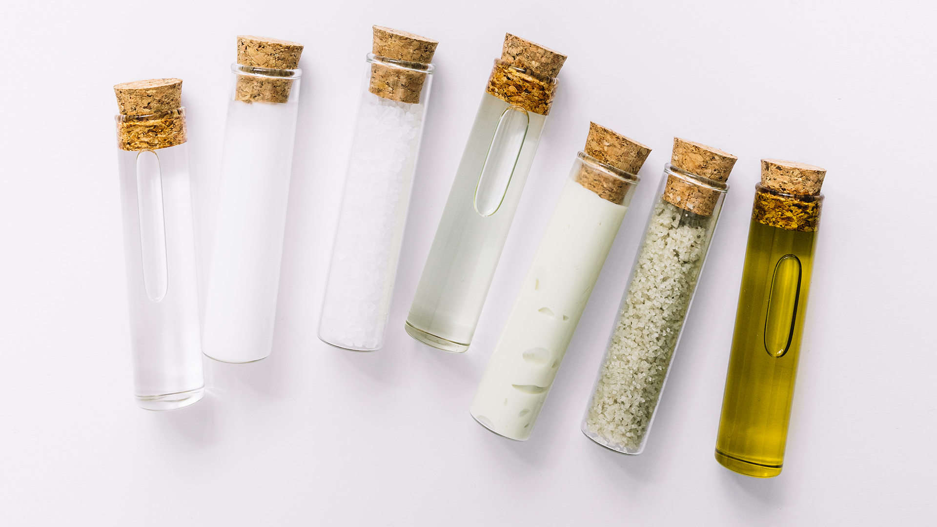 Set di provette di vetro con tappo di sughero contenenti liquidi, sali e oli per test cosmetici su sfondo bianco, simbolo del servizio Raw material della business unit cosmetic and medical device di Lifeanalytics
