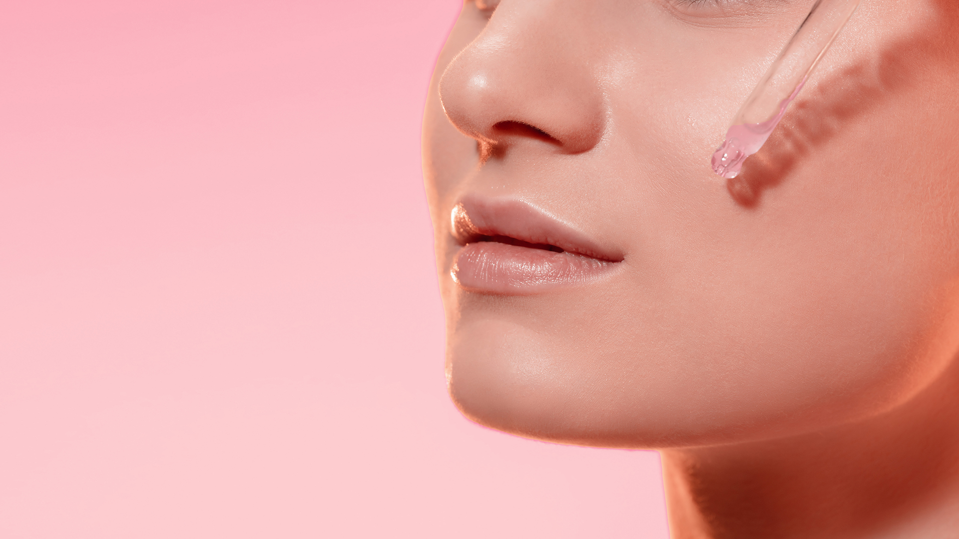Primo piano di una donna con pelle luminosa mentre applica un siero rosa sul viso con un contagocce, su sfondo rosa, simbolo del servizio skincare della business unit cosmetic and medical device di Lifeanalytics