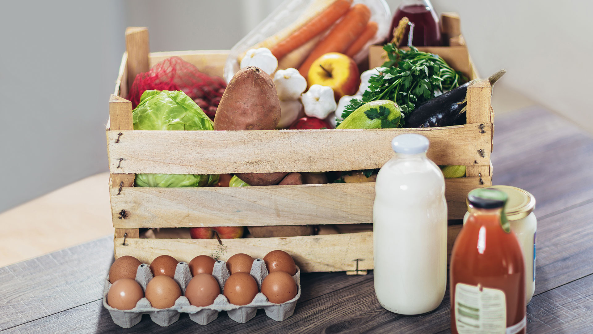 Immagine di una cassetta di legno con alimenti freschi assortiti come verdura, frutta, uova, latte e succhi, simbolo di filiera alimentare e sicurezza alimentare, simbolo del corso dedicato allo standard catena di custodia (CoC) GlobalG.A.P.
