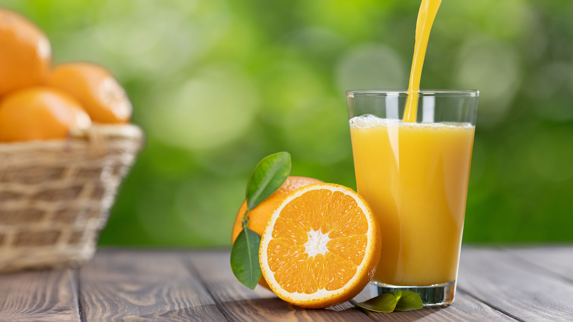 Bicchiere di succo d'arancia fresco con arance intere e tagliate su un tavolo di legno