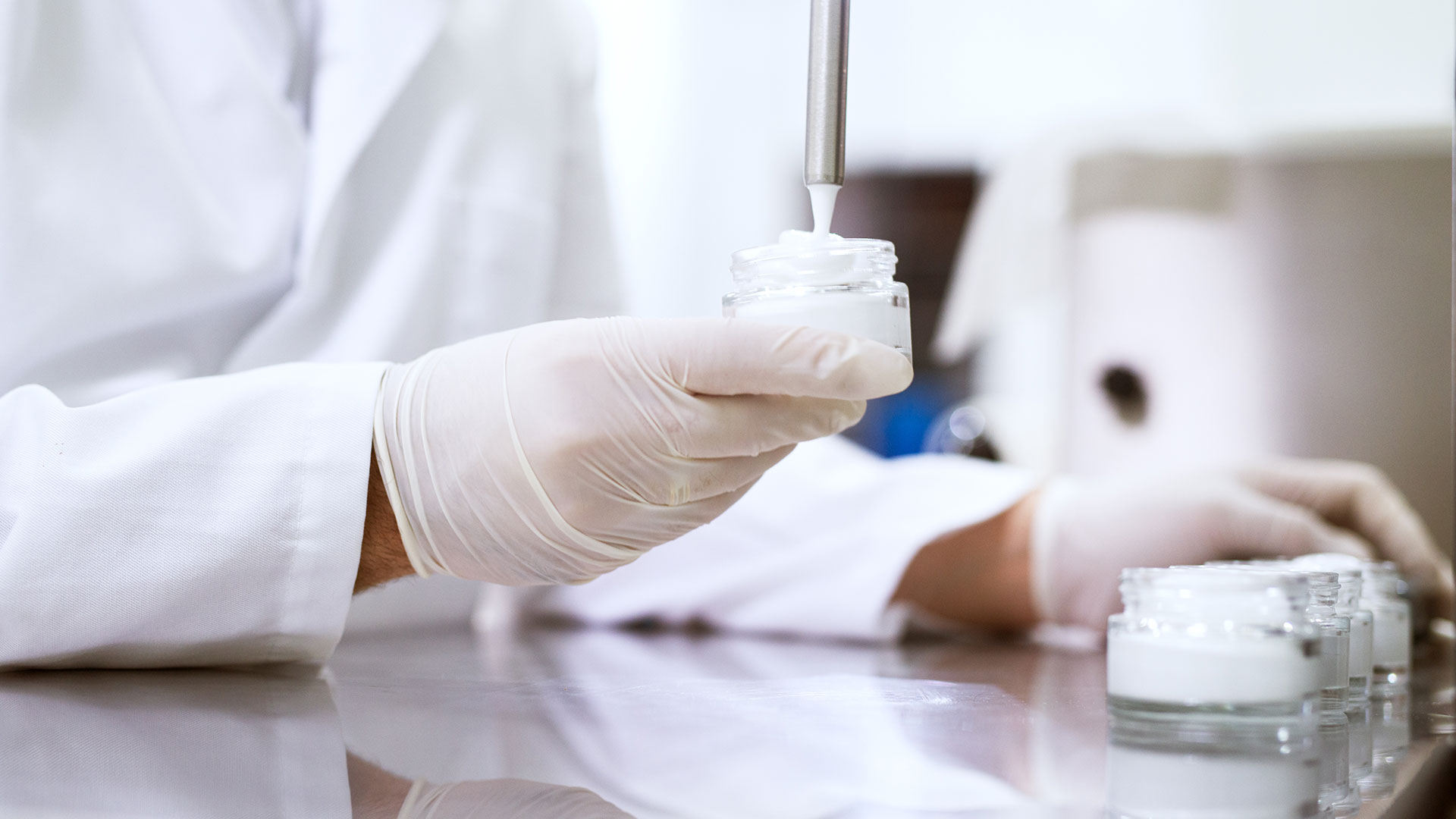 Tecnico di laboratorio che riempie vasetti di crema durante un controllo qualità, simbolo del servizio Suncare della business unit cosmetic and medical device di Lifeanalytics