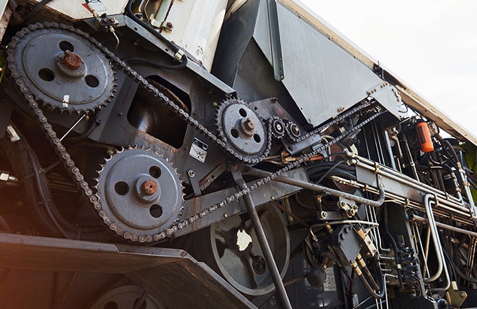 Dettaglio di un macchinario industriale con catene, ingranaggi, pulegge e componenti meccanici in metallo, immagine simbolo dell’articolo dedicato al nuovo regolamento macchine UE 2023/1230 per la business unit EHS di Lifeanalytics