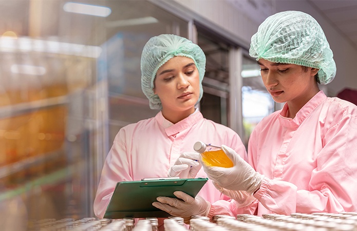 Immagine di due persone che stanno effettuando una serie di tecniche di controllo qualità in stabilimento alimentare verificano un campione di bibita arancione, simbolo dell'articolo del blog Food che tratta la tematica dell'audit integrato per sicurezza e qualità nel settore food