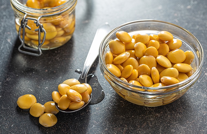 Una ciotola di vetro piena di lupini gialli appoggiata su un piano scuro, con alcuni lupini sparsi accanto a un cucchiaio, simbolo dell’articolo del blog della business unit food sugli Alcaloidi chinolizidinici negli alimenti: cosa sono, rischi e controlli nella filiera