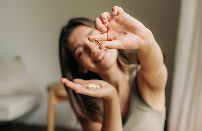Immagine di una donna che mostra una capsula di integratore alimentare con sorriso, focus su benessere e beauty routine, simbolo dell’articolo del blog dedicato ai beauty claim negli integratori alimentari, che cosa sono e cosa dice la legge a riguardo,  della business unit cosmetic & medical device di Lifeanalytics