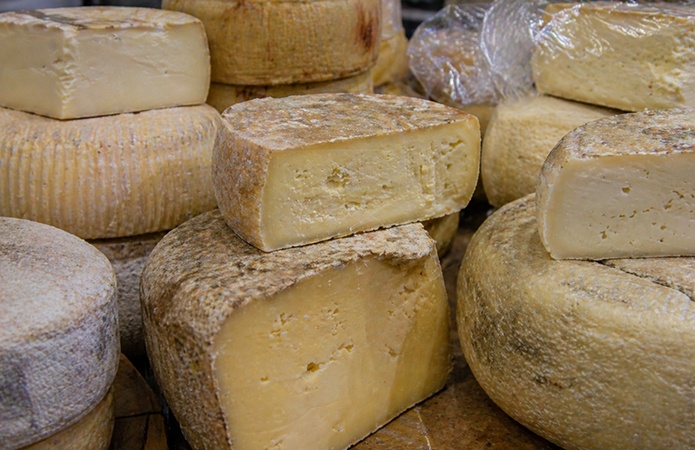 Forme e porzioni di formaggi stagionati disposte su un banco, con crosta naturale e pasta compatta visibile al taglio, simbolo dell'articolo del blog della business unit Food dedicato all'inasprimento delle sanzioni negli illeciti agroalimentari e cosa prevede la nuova Legge GRA/51/2026