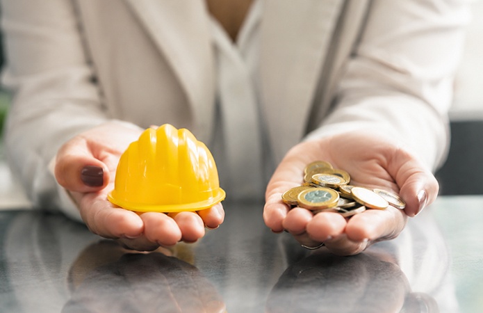 Persona che tiene in una mano un casco di sicurezza giallo e nell'altra alcune monete in euro, immagine simbolica dell'articolo dedicato al Conto Formazione, ai Fondi Interprofessionali e alle opportunità di finanziare la formazione aziendale e gli obblighi in materia di salute e sicurezza della business unit EHS