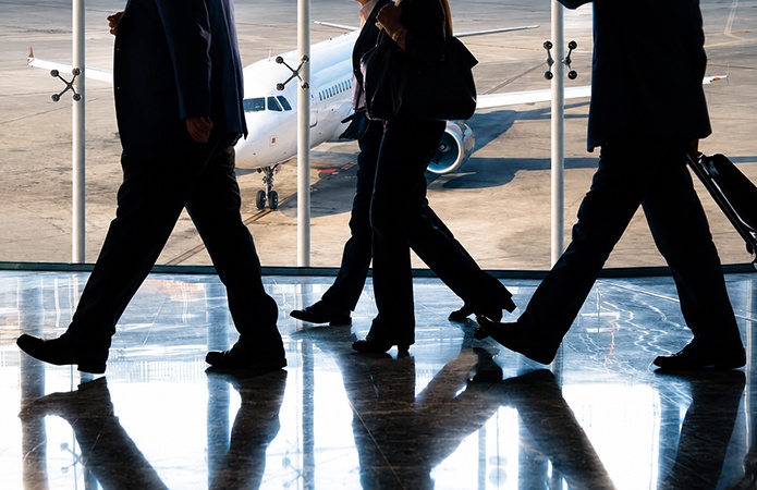 Professionisti in viaggio d’affari all’interno di un aeroporto con aereo sullo sfondo, immagine simbolica dell’articolo della business unit EHS dedicato al Travel Risk Management, alla gestione dei rischi nelle trasferte di lavoro e alla tutela della sicurezza dei lavoratori secondo la ISO 31030:2021
